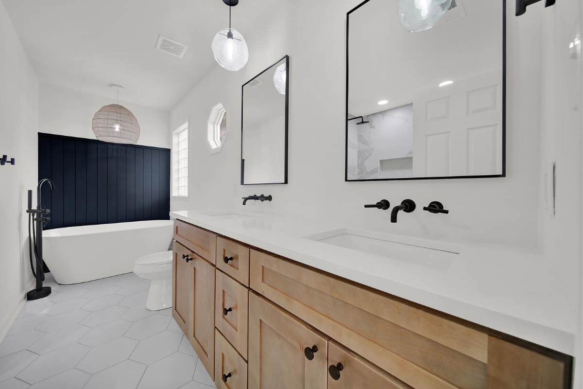 Modern bathroom with light wood vanity, white countertop, black fixtures, and freestanding tub