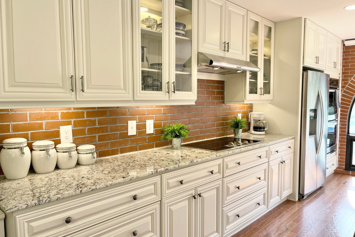 White kitchen cabinets with glass doors, granite countertops, brick backsplash, and stainless steel appliances