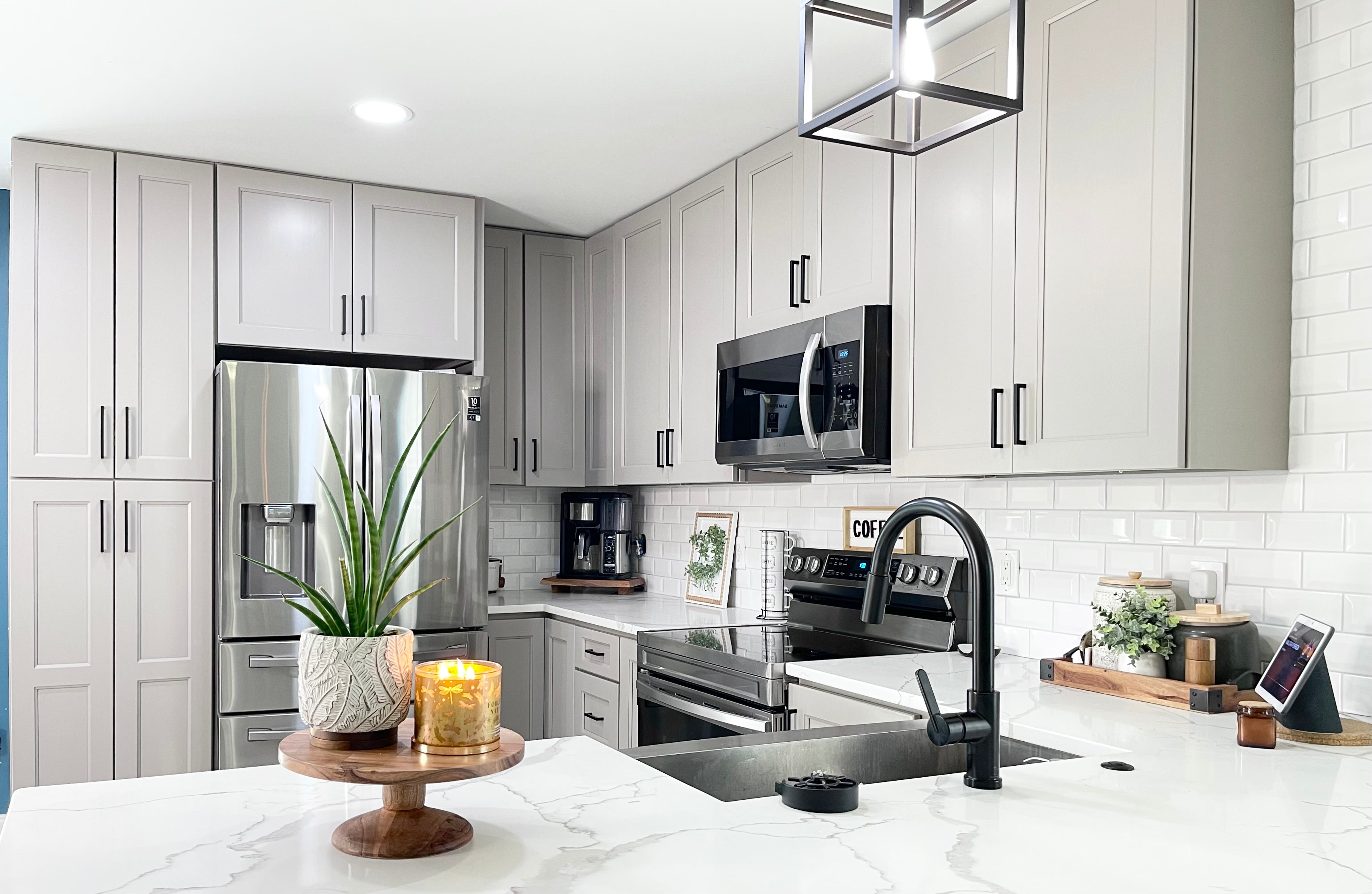 Modern kitchen with white shaker cabinets, marble countertops, stainless steel appliances, and black hardware